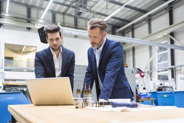 Two men at table in factory using laptop - DIGF02097