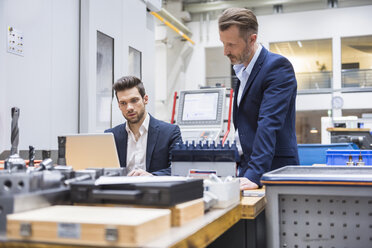 Zwei Männer an einem Tisch in einer Fabrik mit Laptop - DIGF02099