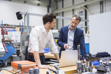 Zwei Männer am Tisch in einer Fabrikhalle mit Laptop - DIGF02100