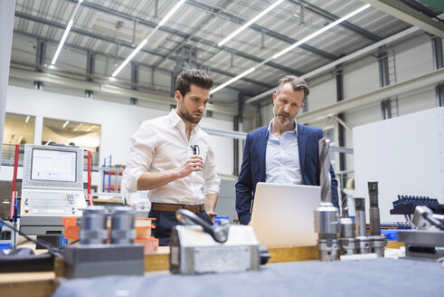 Two men at table in factory shop floor looking at laptop - DIGF02101