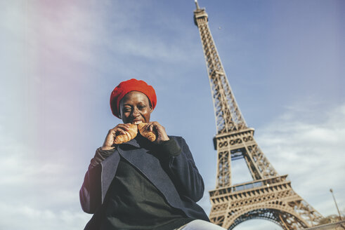 Frankreich, Paris, junge Frau isst zwei Croissants vor dem Eiffelturm - KIJF01385