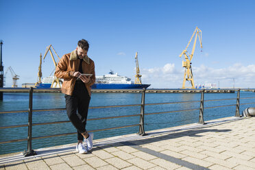 Spanien, Cadiz, Junger Mann am Hafen mit digitalem Tablet - KIJF01389