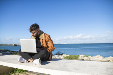 Spanien, Cadiz, Junger Mann am Hafen mit Laptop - KIJF01390