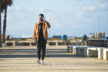 Spain, Cadiz, Young man at the harbour talking on the phone - KIJF01392