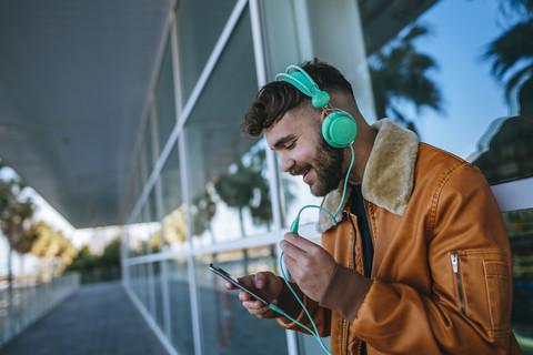 Spain, Cadiz, Young man at the harbour using smartphone, wearing headphones stock photo