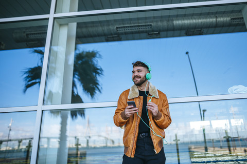 Spanien, Cadiz, Junger Mann am Hafen mit Smartphone, Kopfhörer, lizenzfreies Stockfoto