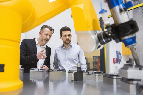 Zwei Geschäftsleute, die Industrieroboter in einer Fabrik beobachten, lizenzfreies Stockfoto