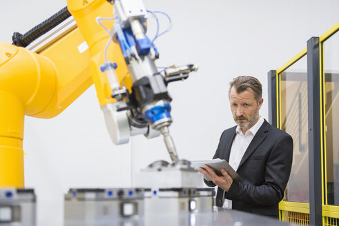 Mature businessman controlling industrial robots with digital tablet - DIGF02111