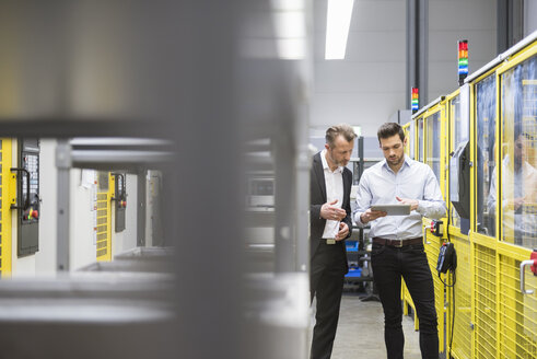 Zwei Geschäftsleute, die Industrieroboter in einer Fabrik beobachten - DIGF02122