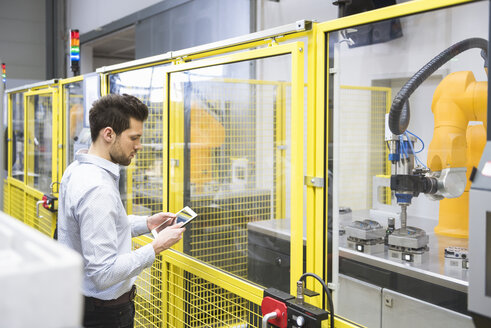 Junger Geschäftsmann bei der Kontrolle der automatisierten Produktion in einer Fabrik - DIGF02124