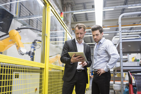 Zwei Geschäftsleute, die Industrieroboter in einer Fabrik beobachten - DIGF02130