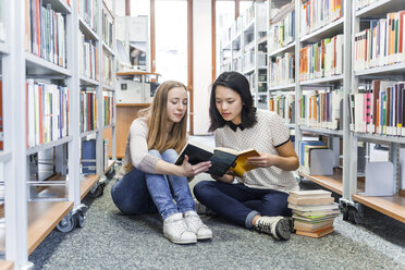 Zwei Mädchen im Teenageralter, die in einer öffentlichen Bibliothek auf dem Boden sitzen und in einem Buch lesen - TCF05379