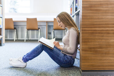 Teenager-Mädchen sitzt auf dem Boden in einer öffentlichen Bibliothek und liest ein Buch - TCF05382