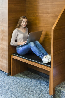 Lächelndes jugendliches Mädchen mit Laptop in einer öffentlichen Bibliothek - TCF05384