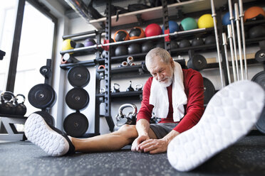 Erschöpfter älterer Mann, der nach dem Training im Fitnessstudio auf dem Boden sitzt - HAPF01528