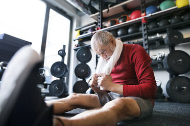 Erschöpfter älterer Mann, der nach dem Training im Fitnessstudio auf dem Boden sitzt - HAPF01529