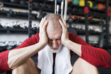 Erschöpfter älterer Mann, der nach dem Training im Fitnessstudio auf dem Boden sitzt - HAPF01530