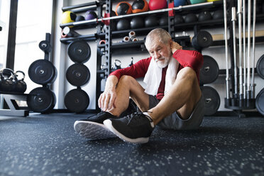 Erschöpfter älterer Mann, der nach dem Training im Fitnessstudio auf dem Boden sitzt - HAPF01531