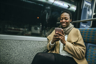 Portrait of smiling young woman looking at cell phone in underground train - KIJF01409