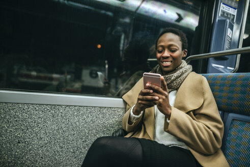 Porträt einer lächelnden jungen Frau, die im U-Bahn-Zug auf ihr Handy schaut - KIJF01409