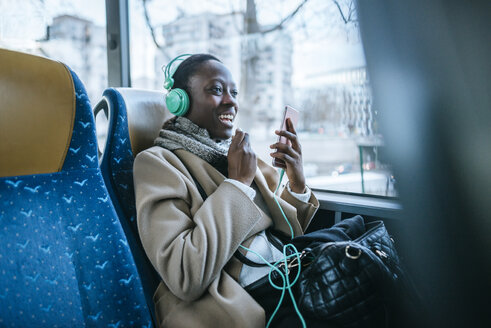 Junge Frau mit Kopfhörern und Smartphone in einem Bus - KIJF01414