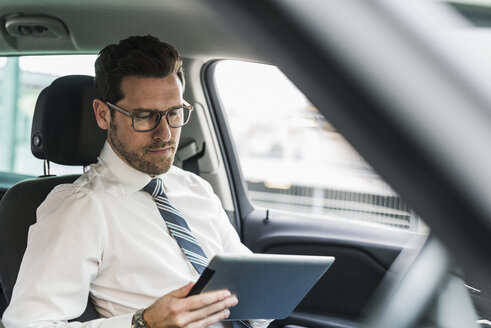 Erfolgreicher Geschäftsmann sitzt im Auto und benutzt ein digitales Tablet - UUF10349