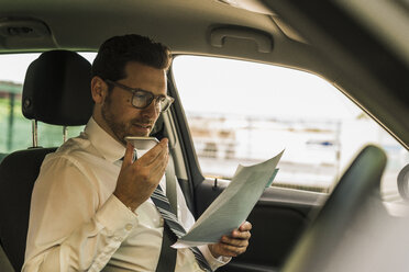 Erfolgreicher Geschäftsmann sitzt im Auto, liest Akten und benutzt sein Smartphone - UUF10352