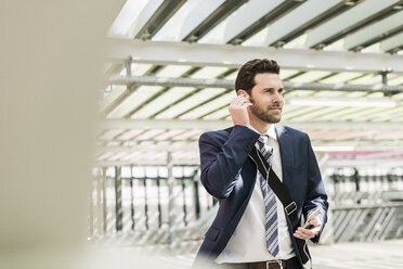 Businessman standing on parking level making a call using earphones - UUF10354