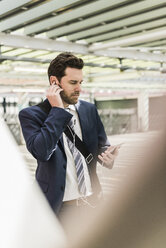 Businessman standing on parking level making a call using earphones - UUF10355