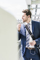 Businessman standing on parking level making a call using earphones - UUF10356