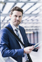 Businessman standing on parking level holding digital tablet - UUF10360