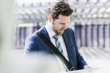 Businessman standing on parking level, reading on digital tablet - UUF10361