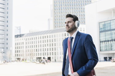 Businessman walking in the city, wearing headphones - UUF10370