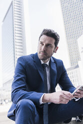 Businessman sitting in the city using smart phone - UUF10371