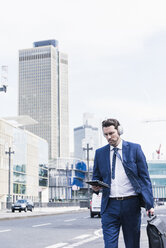 Businessman walking in the city, wearing headphones - UUF10373