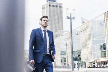 Businessman walking in the city, wearing headphones - UUF10374