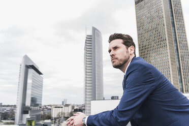 Businessman in front of skyskrapers, looking pensive - UUF10376