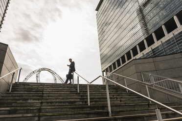 Businessman leaning on railing on top of stairs reading messages - UUF10377