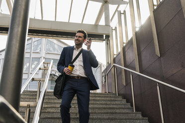 Businessman talking on the phone walking downstairs - UUF10392