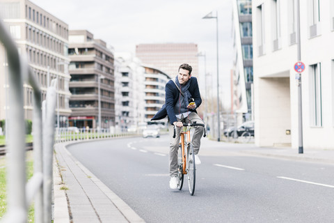 Geschäftsmann fährt mit dem Fahrrad in der Stadt, während er Smartphone und Kopfhörer benutzt, lizenzfreies Stockfoto