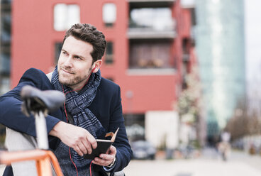 Businessman in the city with bicycle using smartphone and earphones - UUF10405