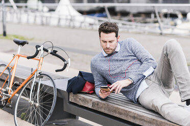 Businessman in the city with bicycle using smartphone and earphones - UUF10410