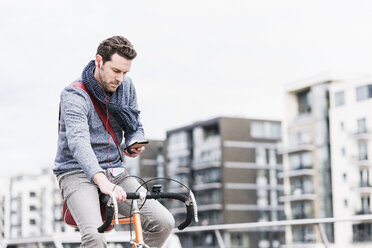 Geschäftsmann fährt mit dem Fahrrad in der Stadt, während er Smartphone und Kopfhörer benutzt - UUF10411