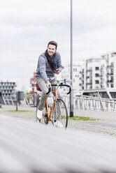 Geschäftsmann fährt mit dem Fahrrad in der Stadt, während er Smartphone und Kopfhörer benutzt - UUF10413