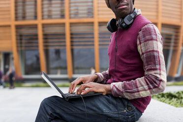 Mann mit Kopfhörern sitzt auf einer Bank und benutzt einen Laptop, Teilansicht - MAUF01045