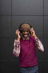 Porträt eines lächelnden Mannes, der mit Kopfhörern und Mobiltelefon Musik hört - MAUF01062