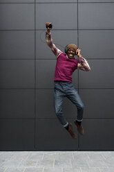 Mann, der in die Luft springt, während er mit Kopfhörern und Mobiltelefon Musik hört - MAUF01065
