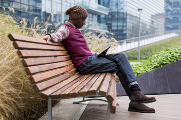 Mann sitzt auf einer Bank und schaut auf ein Tablet - MAUF01068