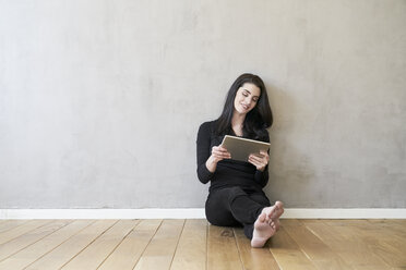 Smiling young woman sitting on the floor using tablet - FMKF03979