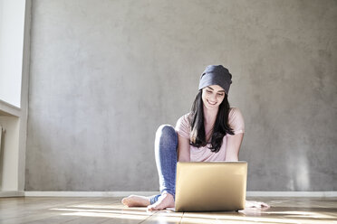 Smiling young woman sitting on the floor using laptop - FMKF03983